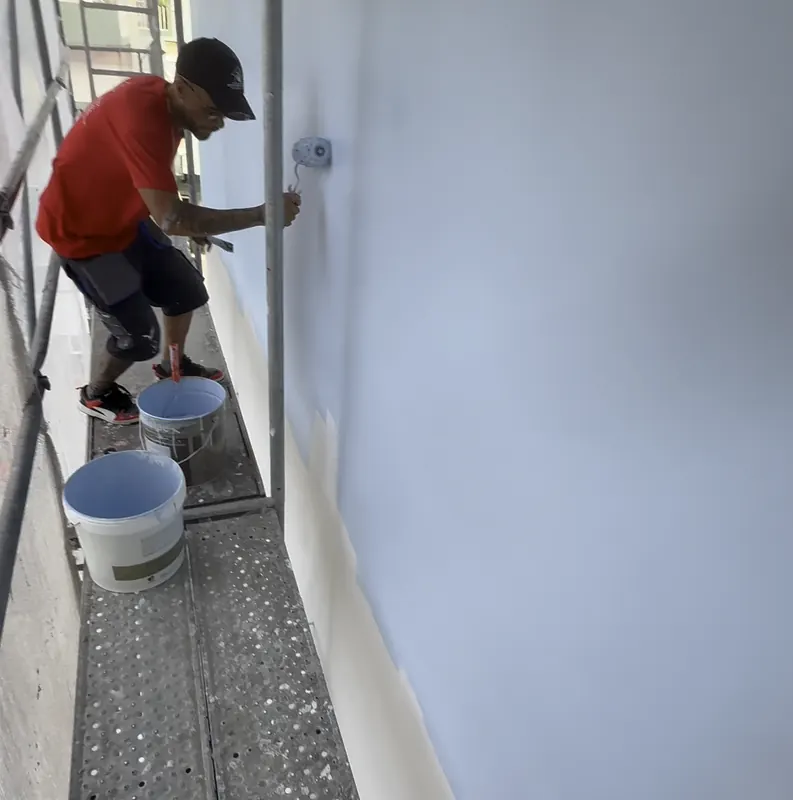 Pintor no andaime a aplicar tinta azul clara com rolo