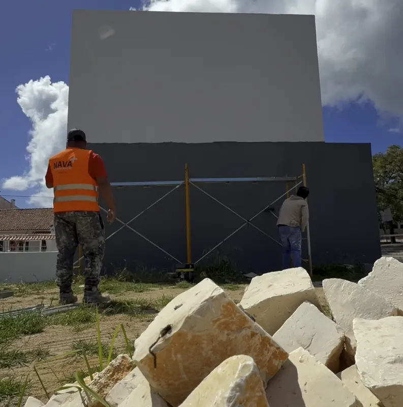 Dois pintores num andaime a pintar a fachada cinzenta de uma moradia
