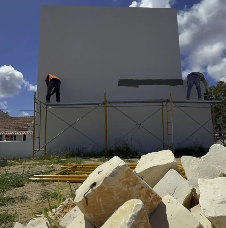 Dois pintores no topo do andaime a pintar a parede cinzenta