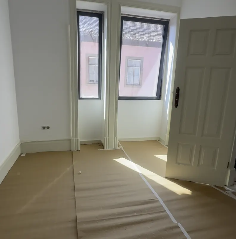 Sala branca com duas janelas e chão coberto com papel de proteção