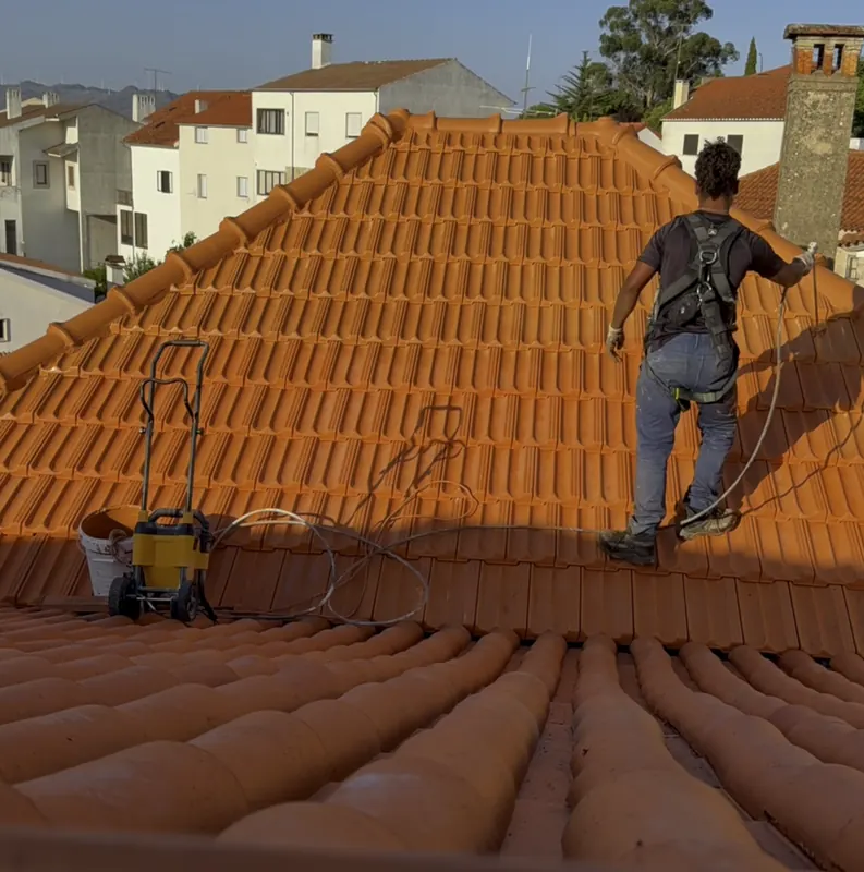 Trabalhador em cima do telhado a pintar as telhas com máquina airless